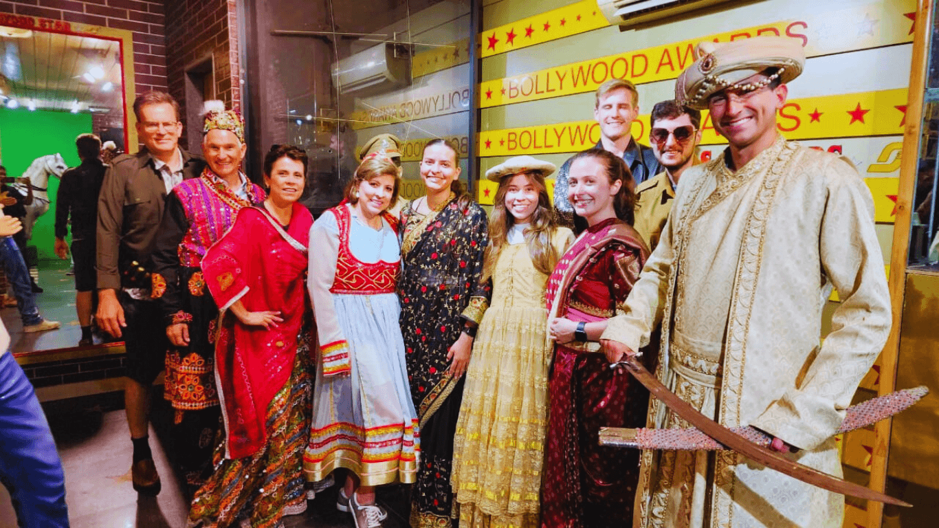 International tourists dressed in traditional Indian costumes posing with Bollywood actors on a movie studio set