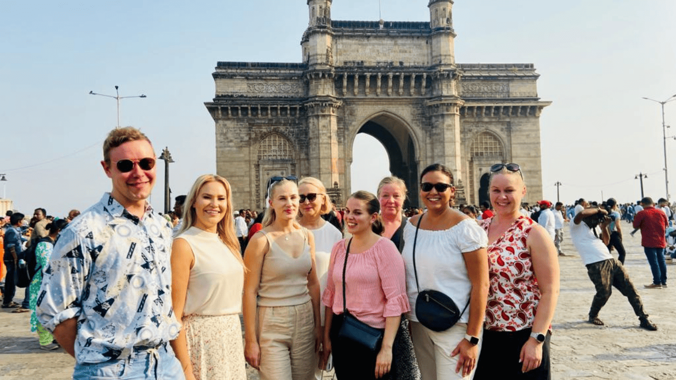 Independent shore excursions takes around a Group of international travelers posing together in front of the Gateway of India in Mumbai during a guided City Tour.