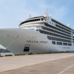 The luxury cruise ship Silver Spirit docked at a port under a clear daytime sky.