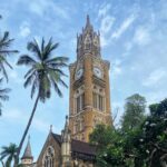 Historic Gothic-style church tower surrounded by palm trees under a blue sky on Elephanta Island, Mumbai.